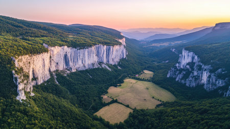 Witness a stunning aerial view of majestic cliffs at sunset, overlooking a lush green valley. This serene landscape captures the beauty of natureの素材