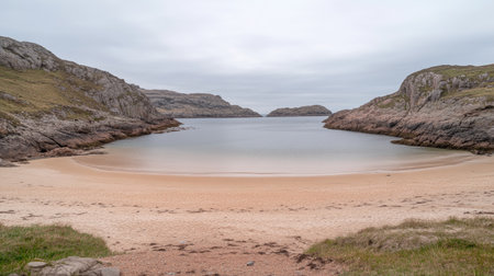 This image captures a serene coastal landscape featuring an empty beach with soft sand, rocky formations, and calm waters under a cloudy sky, perfect for relaxation.の素材