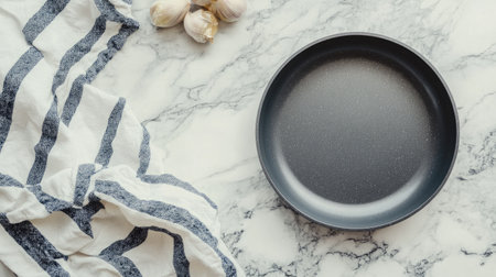 A minimalist black plate rests on a marble countertop, surrounded by fresh garlic and a striped kitchen towel, creating an elegant cooking scene.の素材