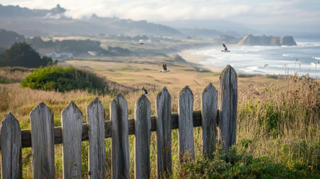 A picturesque coastal scene featuring a rustic wooden fence, birds flying gracefully, and a lush landscape that embodies tranquility and natural beauty.の素材