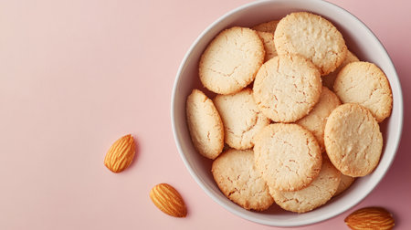 A round bowl filled with freshly baked almond cookies rests on a pink background, creating a colorful and appetizing visual perfect for dessert enthusiasts or food publications.の素材