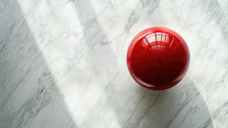 A vibrant red sphere rests on a white marble surface, capturing natural light. The interplay of shadows and reflections adds depth and elegance to the composition.の素材