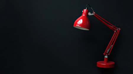 A striking modern red desk lamp positioned against a dark wall, showcasing its sleek design and vibrant color. Perfect for adding style and warmth to any workspace or interior setting.の素材