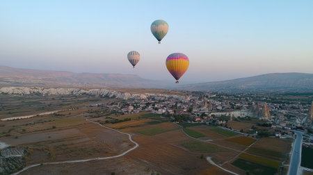 Vibrant hot air balloons soar above the captivating landscape of Cappadocia at sunrise, showcasing the beauty of nature and adventure in a stunning aerial view.の素材