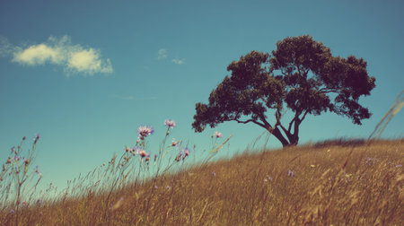 A beautiful solitary tree stands tall on a sunny hill, surrounded by colorful wildflowers and a clear blue sky, creating a serene and peaceful natural landscape.の素材