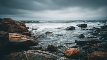 This image captures a tranquil coastal scene with dark clouds overhead, showcasing rolling waves crashing against the rocky shoreline during dusk.の素材