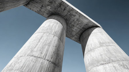 A striking image of massive concrete pillars supporting a flat beam, captured from an upward angle against a vast blue sky, emphasizing architectural beauty.の素材