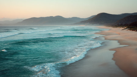 Experience the tranquility of a serene coastal landscape at dusk, where gentle waves caress a sandy beach against a backdrop of distant mountains and a pastel sky.の素材