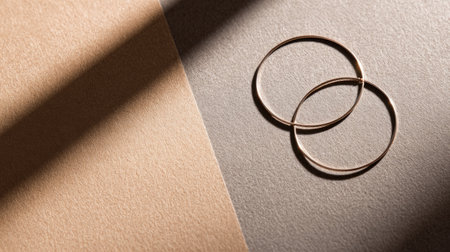 This image showcases two elegant gold hoop earrings on a soft textured background. The interplay of light and shadow enhances the modern aesthetic, perfect for jewelry concepts.の素材
