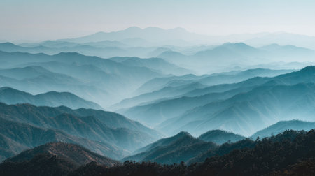 Experience a breathtaking view of misty mountains at dawn, showcasing layers of blue hues and soft light. This serene landscape evokes feelings of tranquility and adventure.の素材