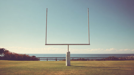 A peaceful scene featuring an empty rugby goal post set against a stunning ocean horizon at sunset, creating a relaxing view in an outdoor sports field.の素材