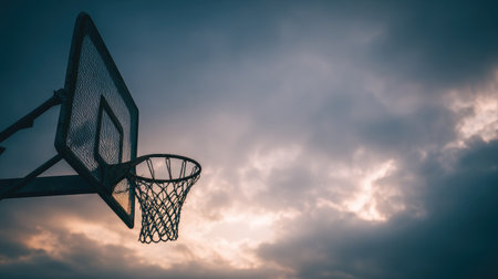 A solitary basketball hoop silhouetted against a moody sky adds an artistic touch to the theme of sports, inviting reflection on athletic endeavors and aspirations.の素材