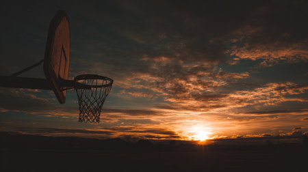 A stunning sunset casts vibrant colors over an empty basketball court, with a hoop silhouetted against a dramatic sky, symbolizing the blend of sport and nature.の素材