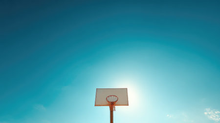 An inviting view of a basketball hoop silhouetted against a clear blue sky with radiant sunlight, symbolizing playfulness and community spirit in sports.の素材