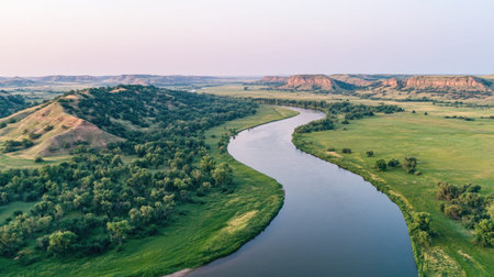 This breathtaking aerial view showcases a meandering river surrounded by lush green fields and rolling hills, creating a serene and picturesque landscape at sunset.の素材