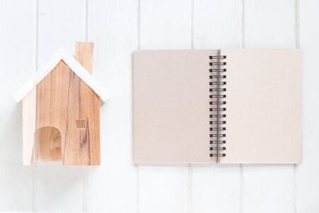 Miniature house model with blank paper notebook on white wood background, copy spaceの写真素材