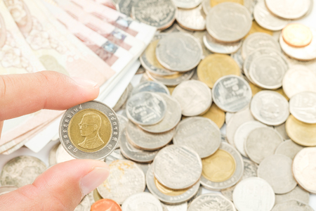 Hand holding thailand ten baht coins with finger by thai coins and bank note behind on white backgroundの写真素材
