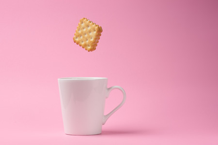 square sandwich cracker falling to coffee cup on pink background with some shadowの写真素材