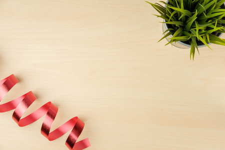 red ribbon spiral and small tree in pot with space on wood table background, top viewの写真素材