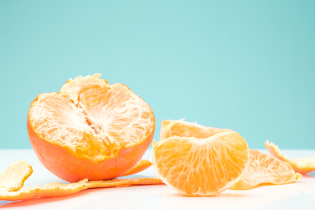 slice and half of orange with orange peel on white table against light green backgroundの写真素材