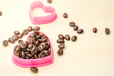 coffee beans in heart shape pink mold on wood tableの写真素材