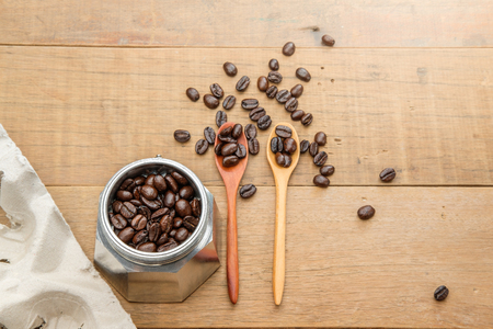 coffee beans on couple of wood spoon and in a moka pot close to a take home tray of coffee cups on wooden tableの写真素材