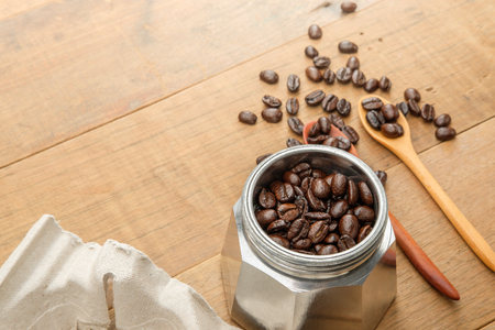 coffee beans on couple wood spoon and in a moka pot close to a take home tray of coffee cups on wooden tableの写真素材