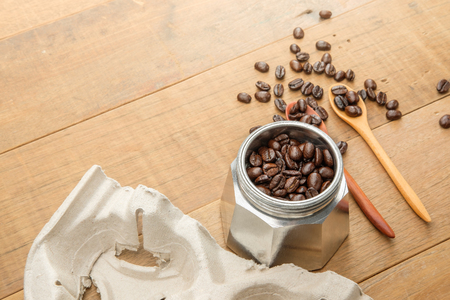coffee beans on couple wood spoon and in a moka pot close to a take home tray of coffee cups on wooden tableの写真素材