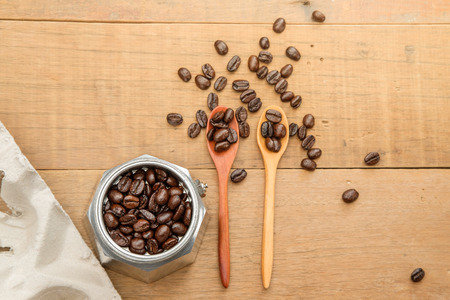 coffee beans on couple wood spoon and in a moka pot close to a take home tray of coffee cups on wooden tableの写真素材