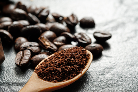 Coffee grounds in wooden spoon close to coffee beans on black graniteの写真素材