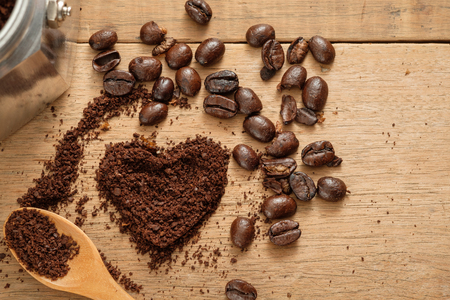 ground coffee in heart shape close to coffee beans on wooden tableの写真素材