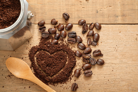 ground coffee in heart shape close to coffee beans on wooden tableの写真素材