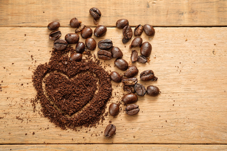ground coffee in heart shape close to coffee beans on wooden tableの写真素材