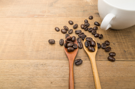 Coffee beans on wood spoon close to white cup over wooden tableの写真素材