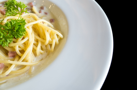 Spaghetti white creamy sauce with ham and mushroom on white dish with black backgroundの写真素材