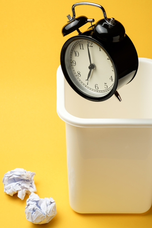 black vintage alarm clock floating on the air from white trash with yellow color backgroundの写真素材