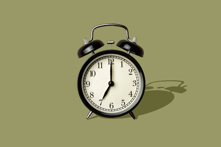 black vintage alarm clock on green color background with long sharp shadowの写真素材