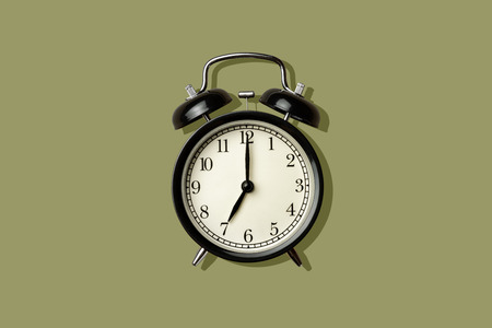 black vintage alarm clock on green color background with sharp shadowの写真素材
