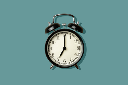 black vintage alarm clock on green color background with sharp shadowの写真素材