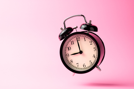 black vintage alarm clock floating on the air with pink color backgroundの写真素材