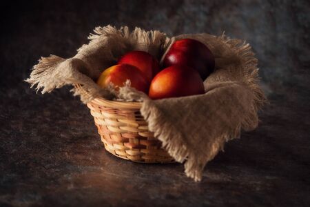 Ripe and juicy nectarines in a basket on a table on a dark background. Rustic style.の写真素材