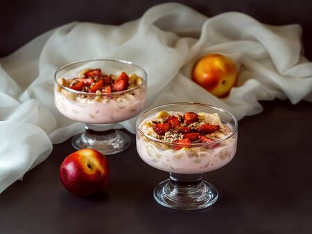 A dessert of yogurt and fruit in glass glasses stands on a dark background decorated with a white clothの写真素材
