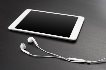 Digital tablet and headphones on a dark table.