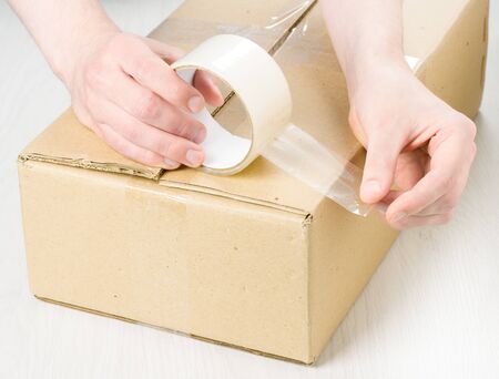 Hands with roll adhesive tape on a cardboxの写真素材