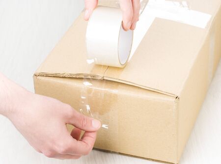 Hands with roll adhesive tape on a cardboxの写真素材