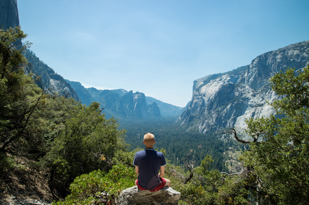 Man sitting looking at Yosemite Valley and lush green forest and mountains in Yosemite National Park, California, USAの写真素材