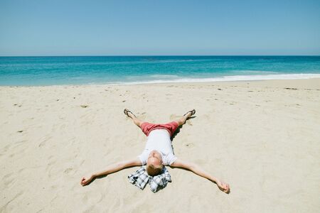 Man relaxing passed out on idyllic tropical beach in starfish position, Pacific Coast highway, California, USAの写真素材