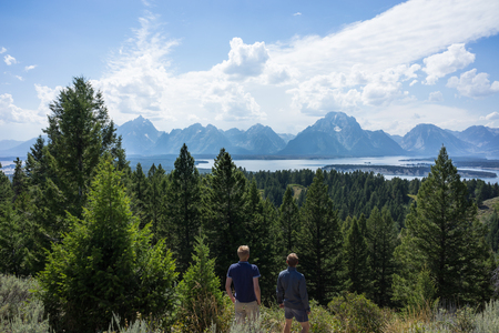 Two friends looking at view of the epic Grand Teton National Park surrounded by lush green forest, lake and natural beauty, United Statesの写真素材