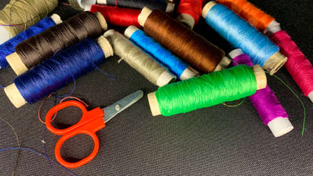 Multi-colored satin threads for sewing wound on spools of different sizes on a black table...