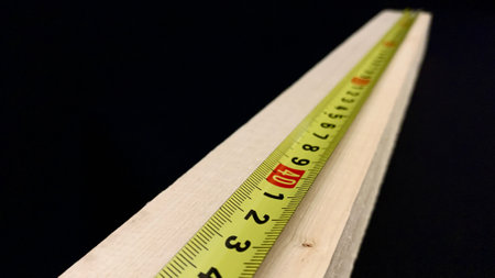 A wooden bar made of fruit wood is measured with a hand tape measure for construction work, the...